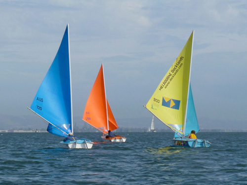 Three brightly colored Access Dinghies sail in the Bay